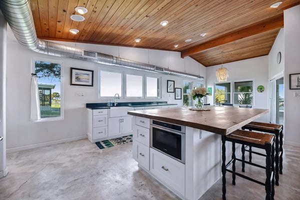 Modern kitchen with white cabinetry, wood island with seating, wood ceiling, and views to outdoor patio area
